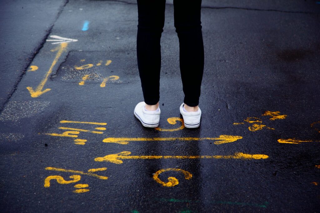 person in black pants and white sneakers standing on black asphalt road
