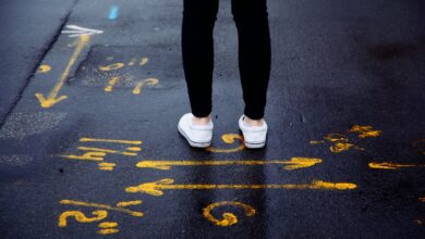 person in black pants and white sneakers standing on black asphalt road