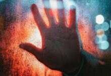A dramatic depiction of a hand pressed against a foggy, illuminated window.